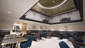Un restaurante con una decoración moderna, que cuenta con un entresuelo, diferentes disposiciones de asientos y un cartel que dice 'The Gold Safe'.
