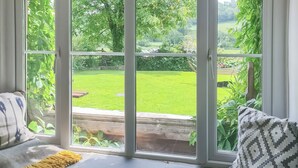 A room with a large window, a bench with cushions, and a view of a green garden. - 4 bedroom accommodation in Llandeilo (Llandeilo)
