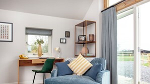 A modern living room with a blue sofa, a wooden desk, and a large window. - 2 bedroom accommodation in Southwood, near Glastonbury (Southwood, near Glastonbury)