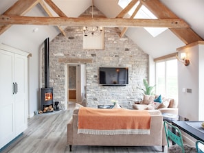 Um quarto estilo loft com vigas de madeira aparentes, parede de pedra, lareira, televisão e um espaço de estar aconchegante.