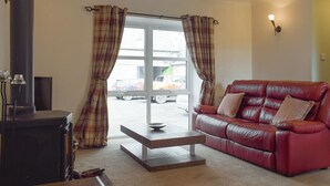 A living room with a red leather sofa, a wooden coffee table, a fireplace, and plaid curtains. - 2 bedroom accommodation in Campsie Fells nr Fintry (Campsie Fells nr Fintry)