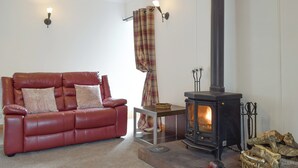 A living room with a red leather sofa, a black wood-burning stove, and a plaid curtain. - 2 bedroom accommodation in Campsie Fells nr Fintry (Campsie Fells nr Fintry)