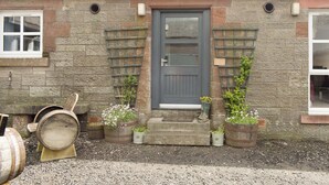 A stone building with a grey door, two windows, and a small porch with potted plants. - 2 bedroom accommodation in Campsie Fells nr Fintry (Campsie Fells nr Fintry)