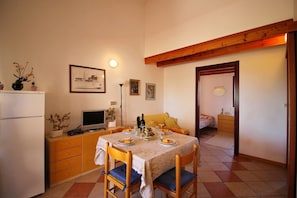 A dining area with a table set for two, a television, and a refrigerator.