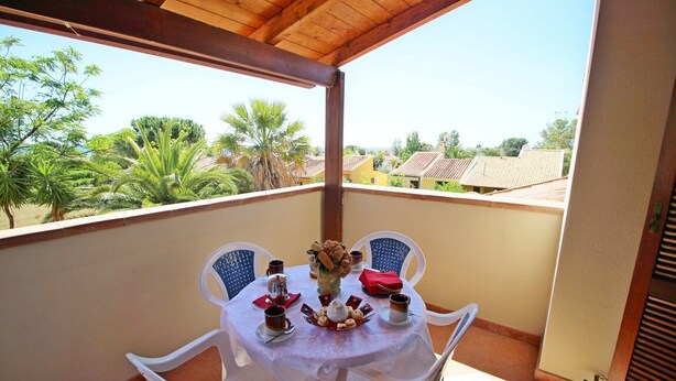 Ein Balkon mit Tisch für zwei Personen, mit Blumen in einer Vase, einer roten Serviette und einer Kaffeekanne.