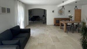 Un salon moderne avec un canapé foncé, un coin repas avec une table et des chaises en bois, et une cuisine en arrière-plan.
