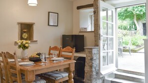 A dining area with a wooden table, chairs, and a vase of flowers. There is a clock on the wall and a framed picture above the table. - Rose Cottage - UK34067 (Grassington)