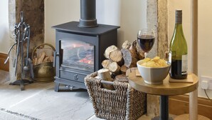 A cozy room with a wood-burning stove, a bowl of chips, a glass of wine, and a bottle of wine on a small table. - Rose Cottage - UK34067 (Grassington)