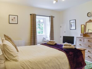 Een slaapkamer met een bed, een dressoir, een televisie en een raam met gordijnen.