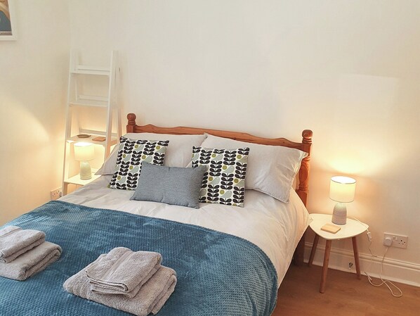 A neatly made bed with patterned pillows, a blue blanket, and folded towels. There are bedside lamps on either side of the bed.