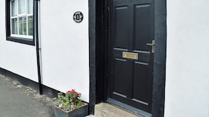 A black door with a brass handle, a white wall, and a window with a black frame. - 3 bedroom accommodation in Embleton (Embleton)
