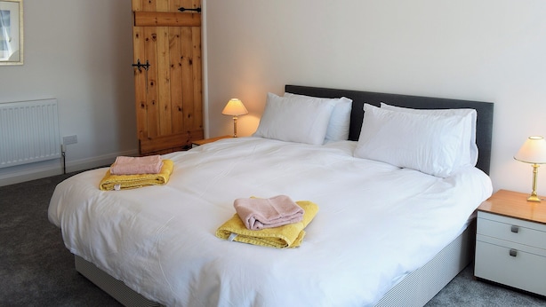 A neatly made bed with white linens, two bedside lamps, and a wooden wardrobe. - 3 bedroom accommodation in Embleton (Embleton)
