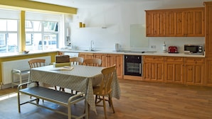 A kitchen with wooden cabinets, a dining table with chairs, a built-in oven, and a window providing natural light. - 3 bedroom accommodation in Embleton (Embleton)