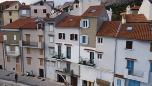 A row of multi-story buildings with balconies, a church with a bell tower, and a rocky hillside in the background. - Studio Apartment Direkt am Strand (Baška)