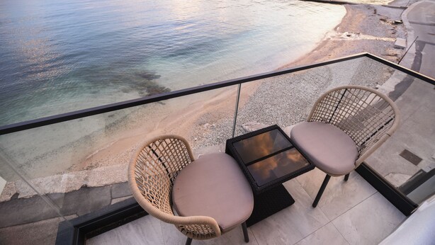 A balcony with wicker chairs and a glass table overlooking a beach. - Studio Apartment Direkt am Strand (Baška)