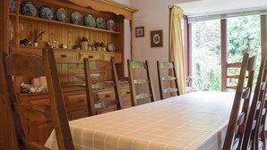 A dining room with a long table, wooden chairs, a wooden cabinet with decorative plates, and a window with curtains.