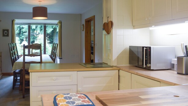A kitchen with a dining area, featuring a wooden table, chairs, a heart-shaped decoration, and a microwave.