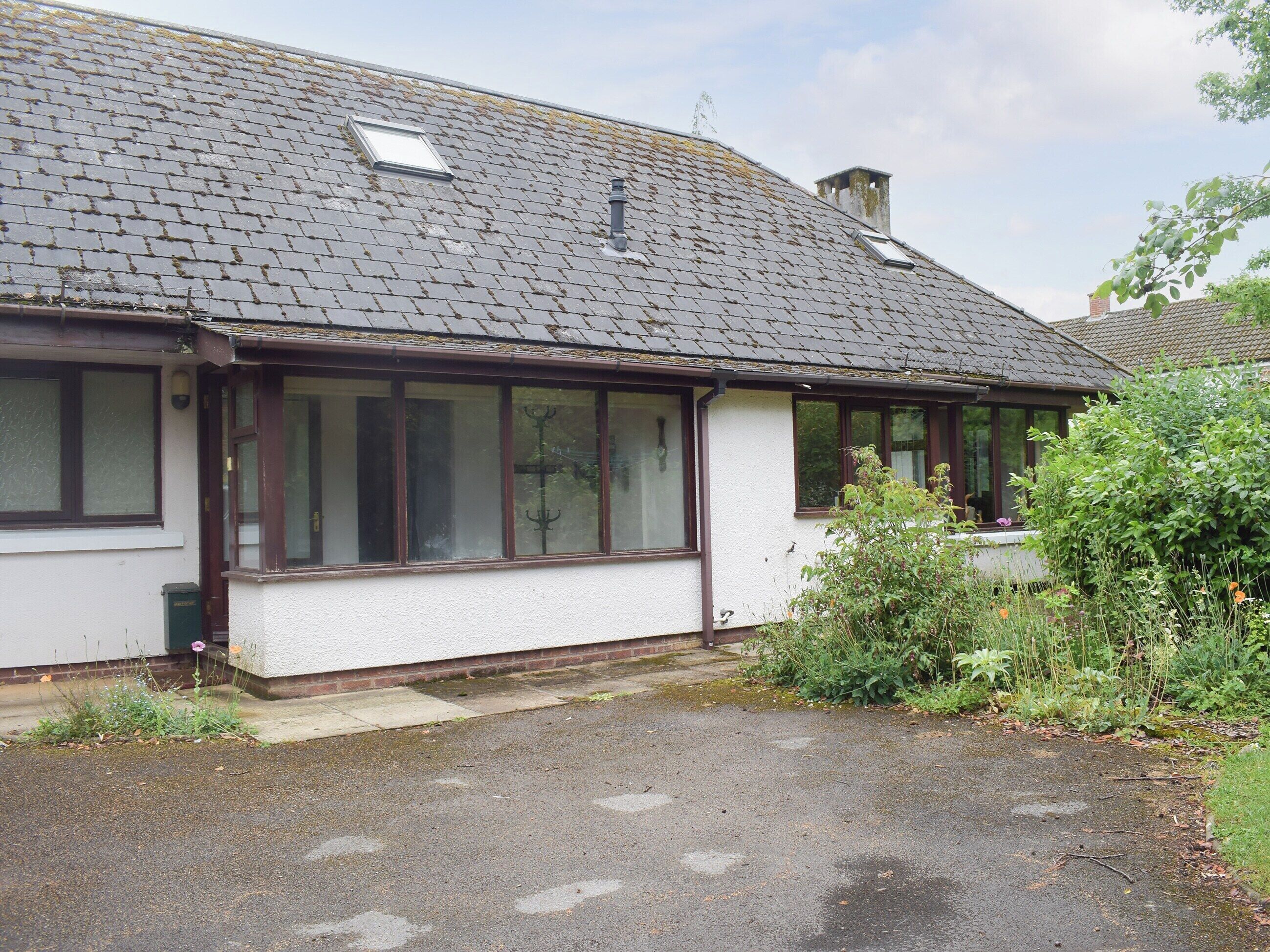 Une maison de plain-pied avec un toit en pente, de grandes fenêtres et un petit jardin.