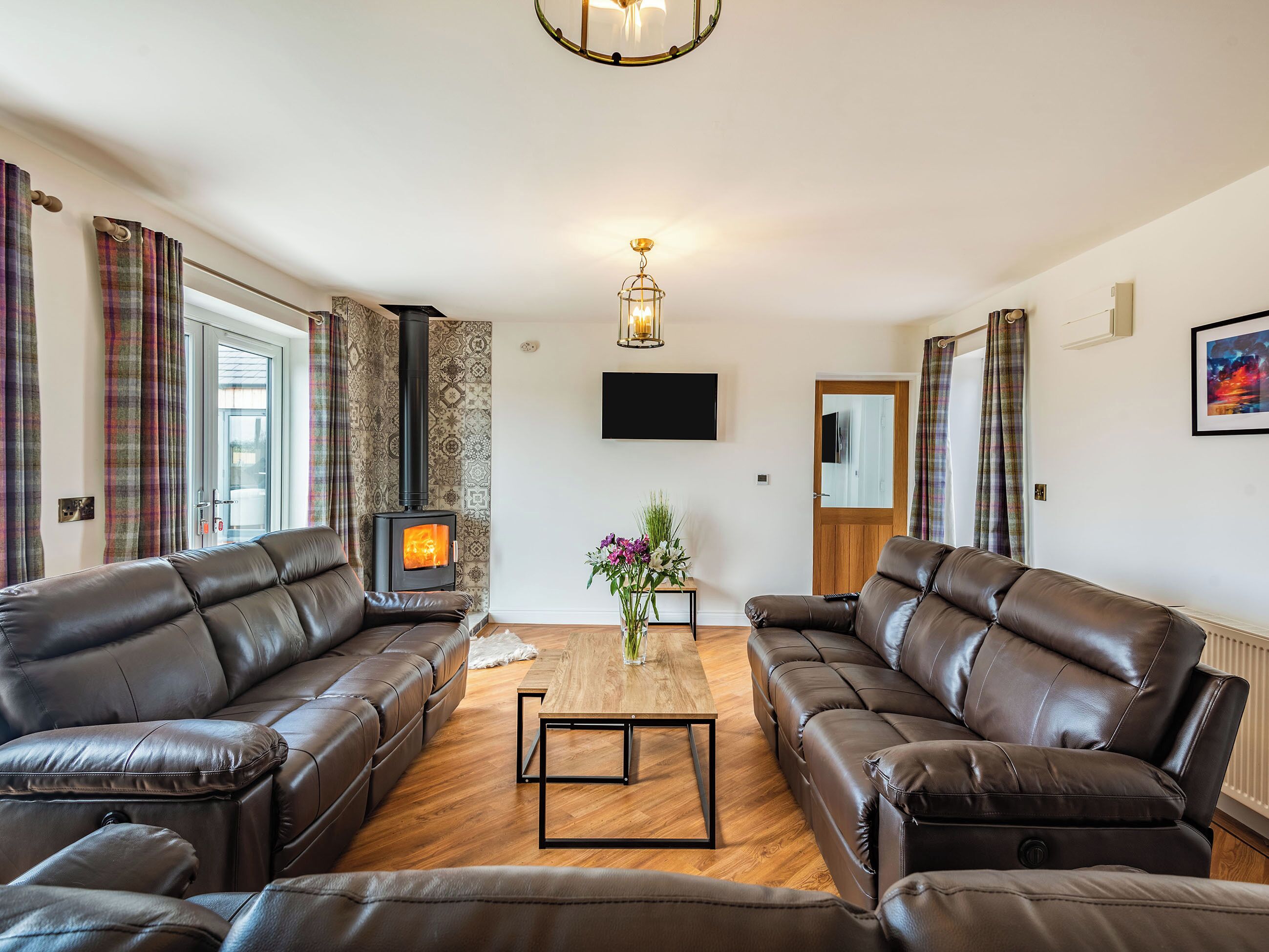 Ein Wohnzimmer mit zwei Ledersofas, einem Holztisch, einem Kamin und einem an der Wand befestigten Fernseher.