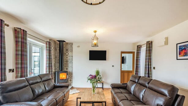 Una sala de estar con dos sofás de cuero, una mesa de centro de madera, una chimenea y un televisor montado.