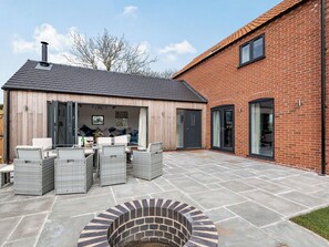 A patio area with wicker furniture, a brick fire pit, and a wooden building with glass doors. - 5 bedroom accommodation in Willoughby, near Alford (Willoughby, near Alford)