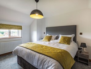 A bedroom with a bed, bedside table, lamp, and a window with a view.