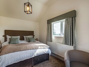 A bedroom with a bed, a bedside table, a lamp, a chair, a window with curtains, and a hanging light fixture. - 5 bedroom accommodation in Willoughby, near Alford (Willoughby, near Alford)