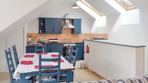 Un'area pranzo con tavolo apparecchiato per quattro, una cucina con mobili blu e un lucernario.