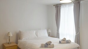 Un letto rifatto con lenzuola bianche, due abat-jour e un comodino in legno con una lampada.