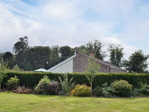 A brick house with a large windowed extension, surrounded by a well-maintained garden and hedges.