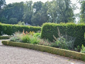 A garden with neatly trimmed hedges, gravel paths, and a variety of flowering plants.