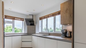 Een moderne keuken met witte kasten, een roestvrijstalen afzuigkap, een inbouwoven, een spoelbak en een koffiezetapparaat.