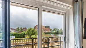 Een balkon met uitzicht op een rivier, een houten hek en gebouwen op de achtergrond.