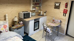 Une cuisine compacte équipée d’un four à micro-ondes, d’un grille-pain et d’un évier. On y trouve également un petit réfrigérateur, un meuble en bois contenant de la vaisselle et une couverture anti-feu accrochée au mur.
