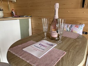 A wooden table with a bottle of Canti Prosecco DOC GROSSECCO DOC GROSSEMENTO, two glasses, and a welcome mat with a message. - Woodlands Lodge - Come and Enjoy the Good Life (Buckley)