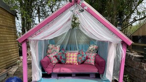 Un espace extérieur accueillant, aménagé avec des couleurs rose et bleu, comprenant un banc rembourré et une petite table.