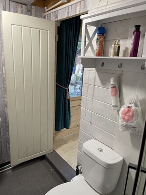 A bathroom with a toilet, a shelf with toiletries, and a curtain. - Woodlands Lodge - Come and Enjoy the Good Life (Buckley)