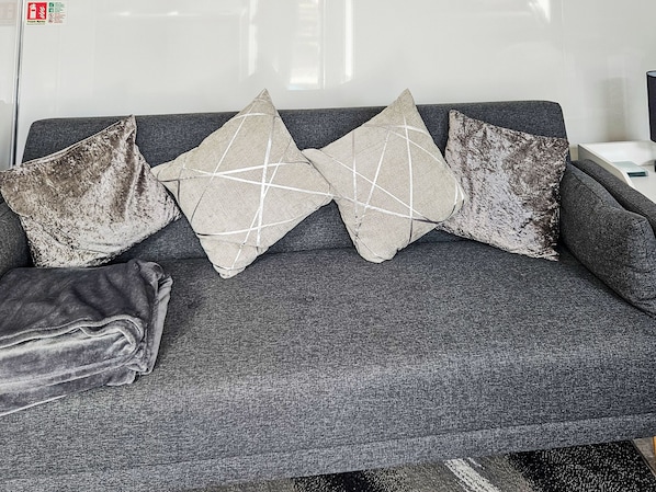 Ein graues Sofa mit drei dekorativen Kissen, eines davon mit einem geometrischen Muster.