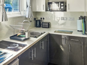 Eine moderne Küche mit integriertem Mikrowellenherd, Toaster und Wasserkocher. Ein Spülbecken mit Geschirrgestell und ein Fenster mit Vorhängen sind vorhanden.