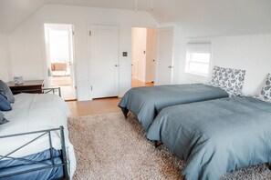 A bedroom with two beds, a wooden floor, white walls, and a door leading to another room.