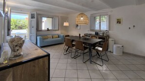 Un salon moderne avec un canapé, une table à manger et des chaises. Une fenêtre offre une vue sur la verdure environnante.