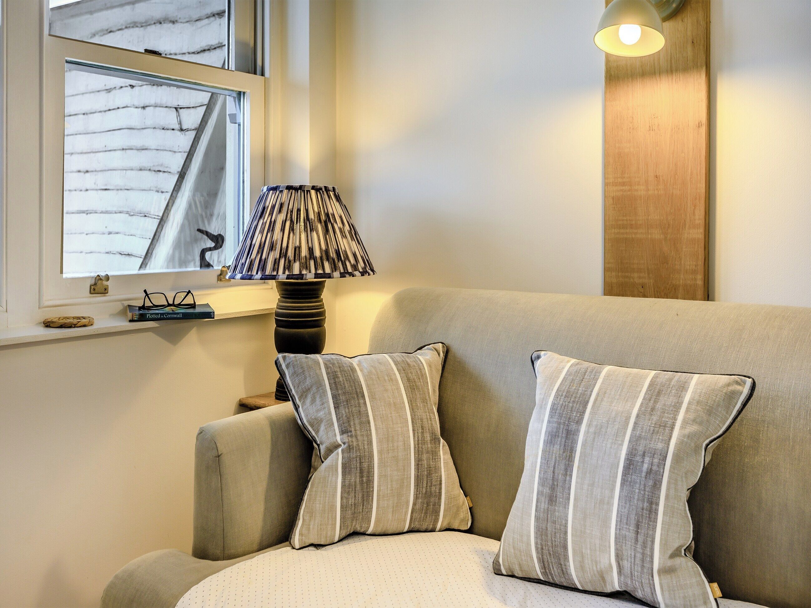 Een gezellige woonkamer met een bank, gestreepte kussens, een lamp en een raam met uitzicht op een gebouw.
