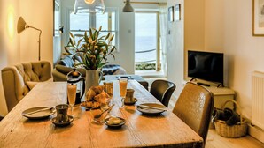 A dining table set with plates, glasses, and a coffee pot, with a view of the sea through a window in the background. - 2 bedroom accommodation in Ilfracombe (Ilfracombe)