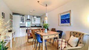 A modern kitchen with white cabinets, a dining table with blue chairs, and a cozy living area with a sofa and a painting. - 2 bedroom accommodation in Ilfracombe (Ilfracombe)