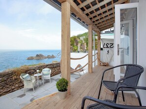 Un espacio al aire libre cubierto con vistas al mar, que cuenta con una pérgola de madera, sillas de mimbre blanco y una silla de metal negro.