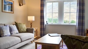 A room with a sofa, a table, a lamp, a painting, and a window with curtains. - Braigh na Leitre - UK33790 (Strathconon, Muir of Ord)