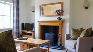 A living room with a fireplace, a television, a coffee table, and two sofas. - Braigh na Leitre - UK33790 (Strathconon, Muir of Ord)