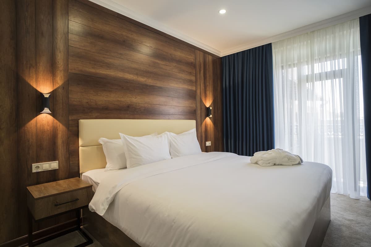 Una cama bien hecha con sábanas blancas, cabecera de madera y dos lámparas fijadas a la pared.
