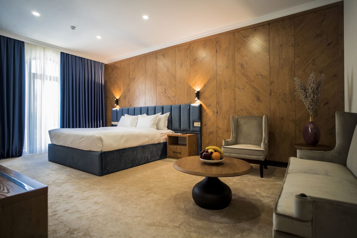 Una habitación de hotel moderna con una cama grande, una mesita de centro redonda con fruta, un sofá y una pared de acento de madera.