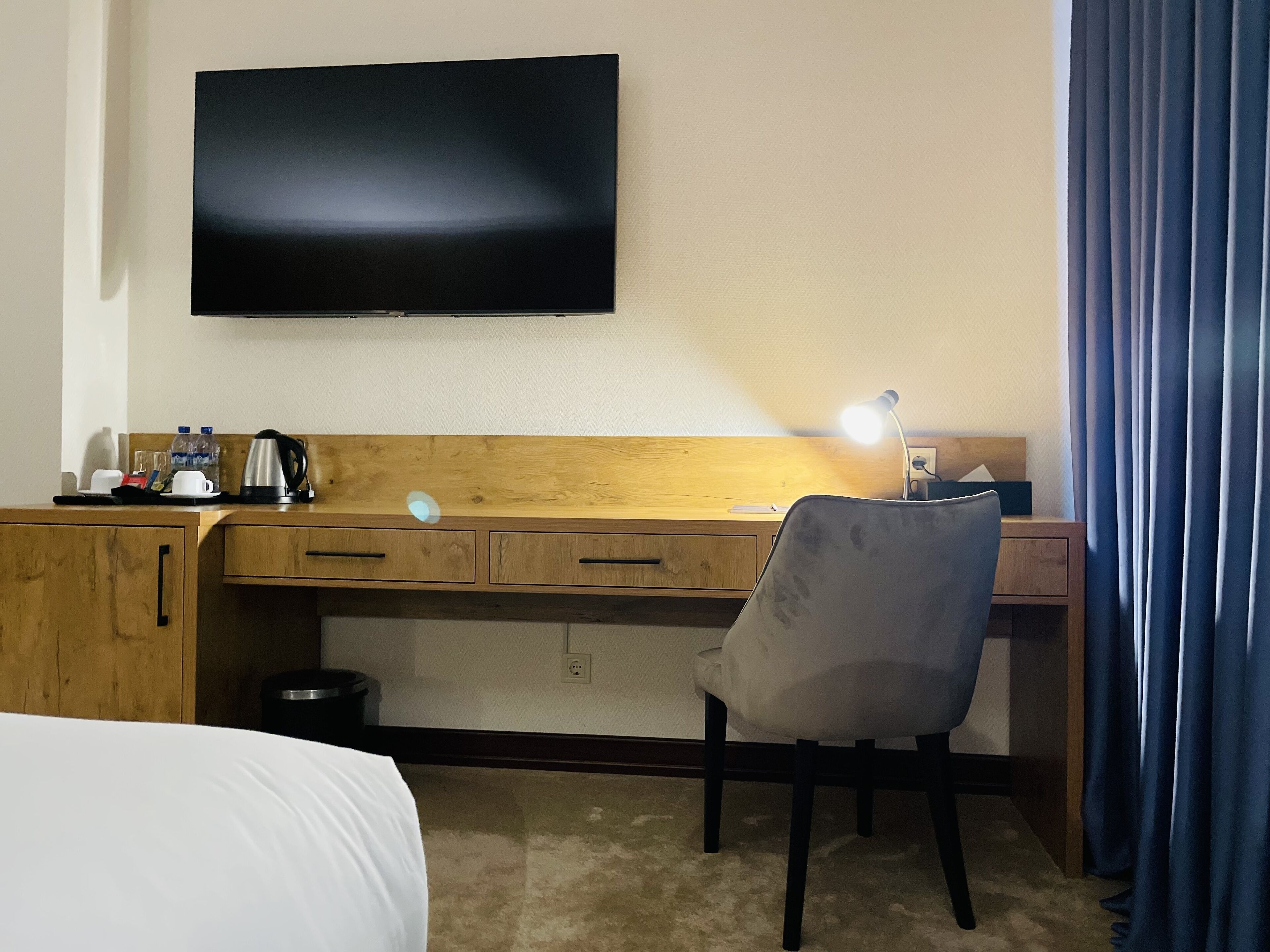 Een hotelkamer met een bed, een bureau met stoel, een televisie en een nachtkastje.